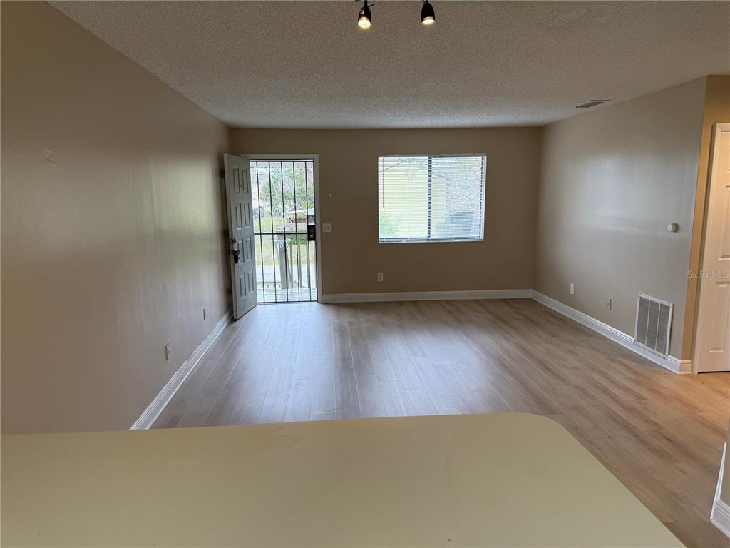 An empty living room features light-colored wood-look flooring, beige walls, and a security screen door — 7340 SWALLOW RUN UNIT 7340, WINTER PARK, FL