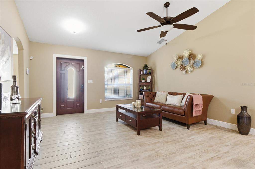 A living room features light wood-look tile flooring, a brown leather sofa, and a ceiling fan — 3018 BARRY ROAD, NORTH PORT, FL