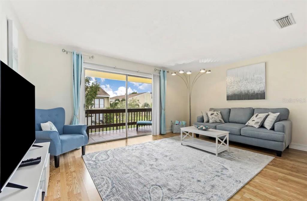 A living room features a blue sofa, matching armchair, white coffee table, and sliding glass doors — 3469 CLARK ROAD UNIT 268, SARASOTA, FL