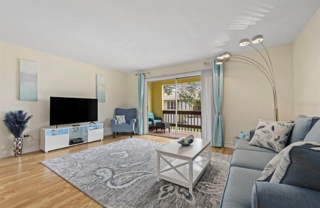 A living room features a blue sofa, a television on a white stand, and a balcony — 3469 CLARK ROAD UNIT 268, SARASOTA, FL