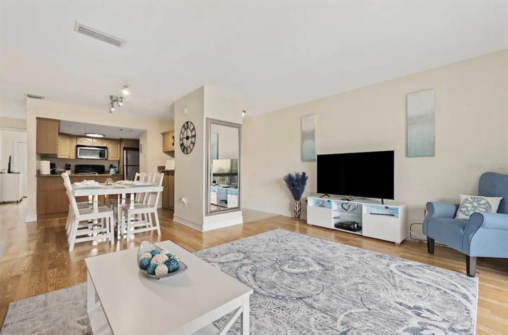 A living room with hardwood floors, a dining area, and a kitchen in the background — 3469 CLARK ROAD UNIT 268, SARASOTA, FL
