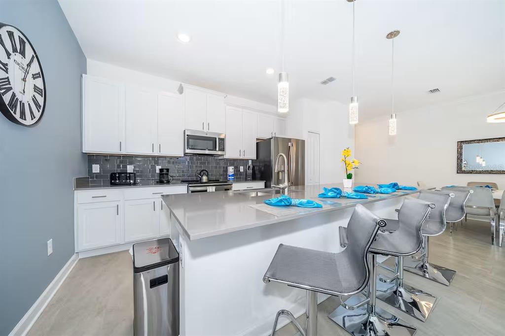 A modern kitchen features white cabinets, gray countertops, a large island, and three bar stools — 4188 PARAGRAPH DRIVE, KISSIMMEE, FL