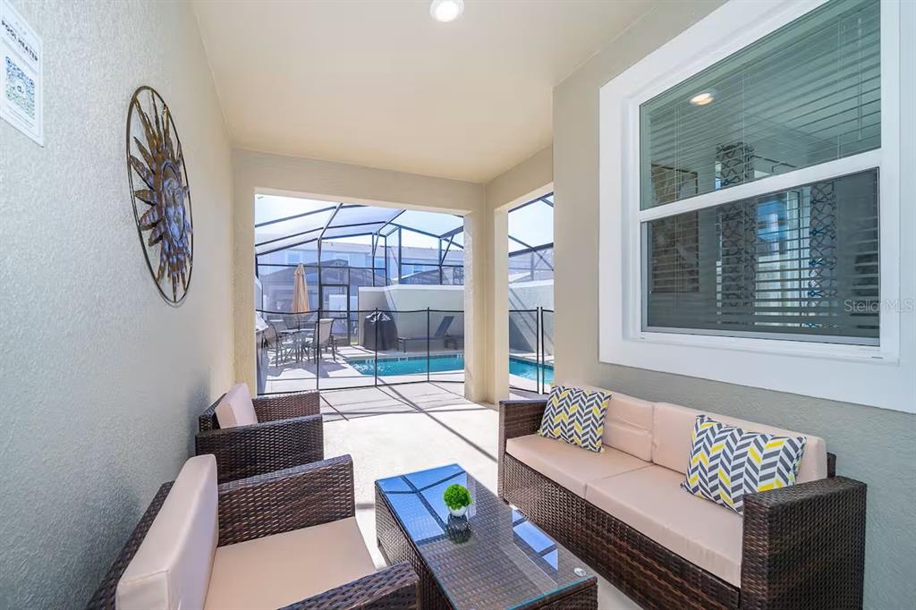 A covered patio features wicker furniture, a glass-top coffee table, and a view of a pool — 4188 PARAGRAPH DRIVE, KISSIMMEE, FL