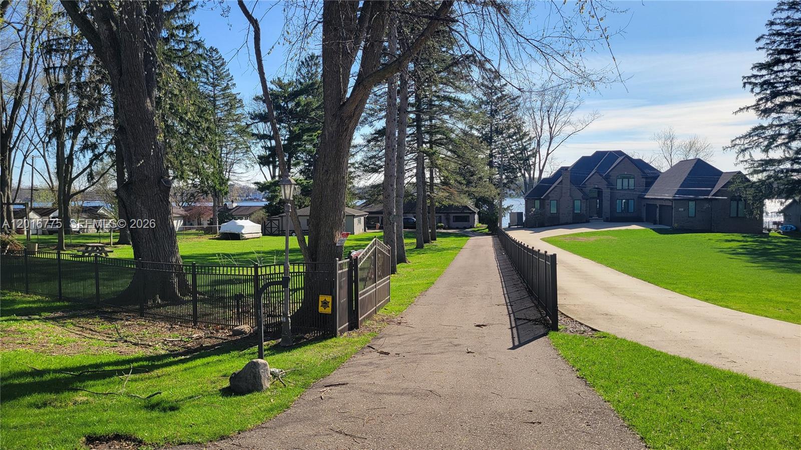 A paved driveway leads toward a large brick house situated on a grassy waterfront lot — 605 Hilltop Drive, MI 48386, MI
