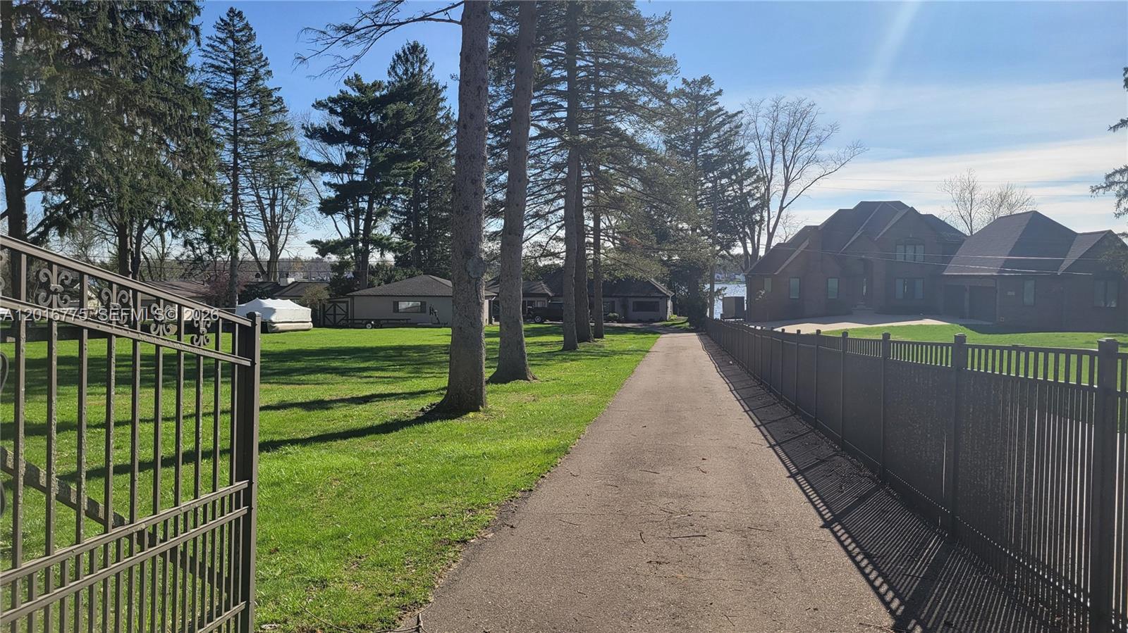 A paved driveway leads toward a house past a grassy lawn and tall pine trees — 605 Hilltop Drive, MI 48386, MI