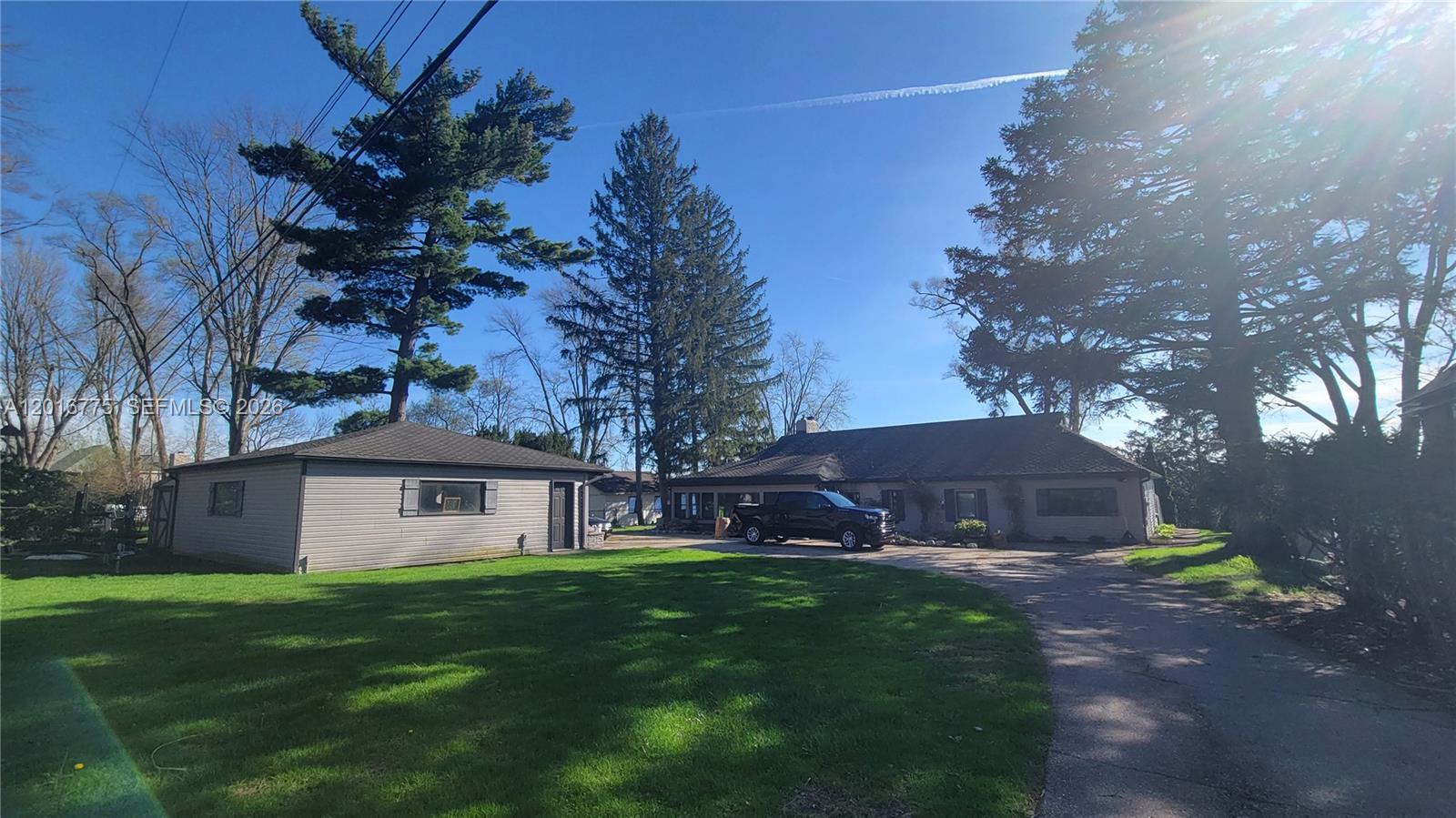 A detached garage and a single-story house sit on a grassy lot with trees — 605 Hilltop Drive, MI 48386, MI
