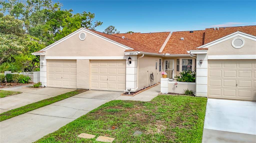 A single-story duplex with beige stucco walls, two garage doors, and a shingled roof — 13130 GREENVIEW COURT, HUDSON, FL