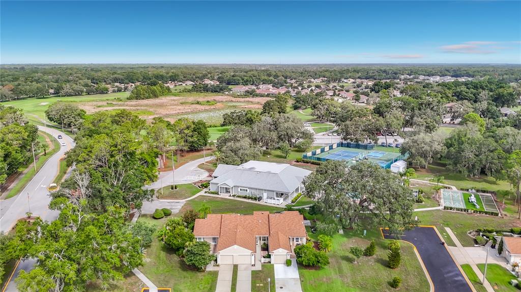 An aerial view shows a residential complex with a clubhouse, tennis courts, and surrounding greenery — 13130 GREENVIEW COURT, HUDSON, FL