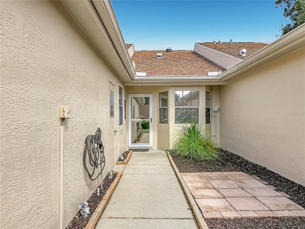 A concrete walkway leads to a front entrance with a storm door and landscaping — 13130 GREENVIEW COURT, HUDSON, FL