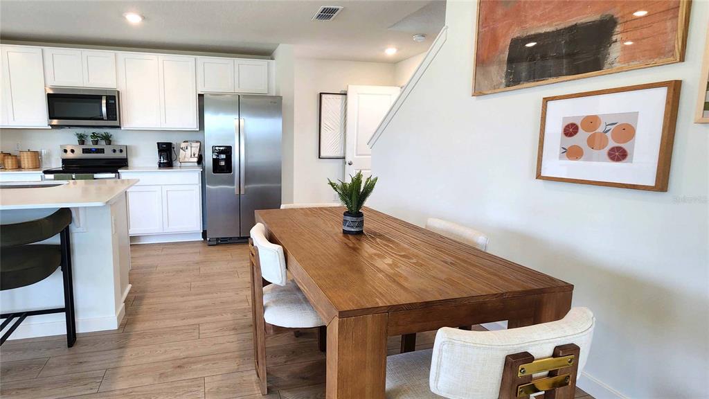 A dining area with a wooden table sits adjacent to a kitchen with white cabinets — 523 REMICK STREET, OSTEEN, FL