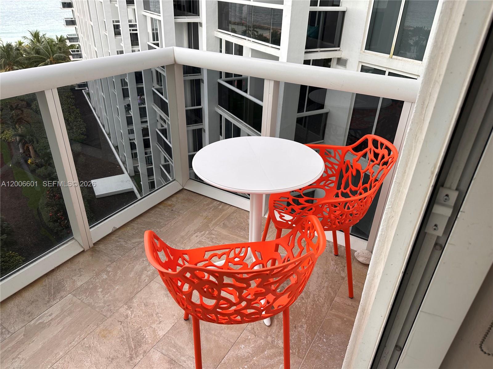 A balcony features a small white table and two orange patterned chairs on tiled flooring — BAL HARBOUR, FL