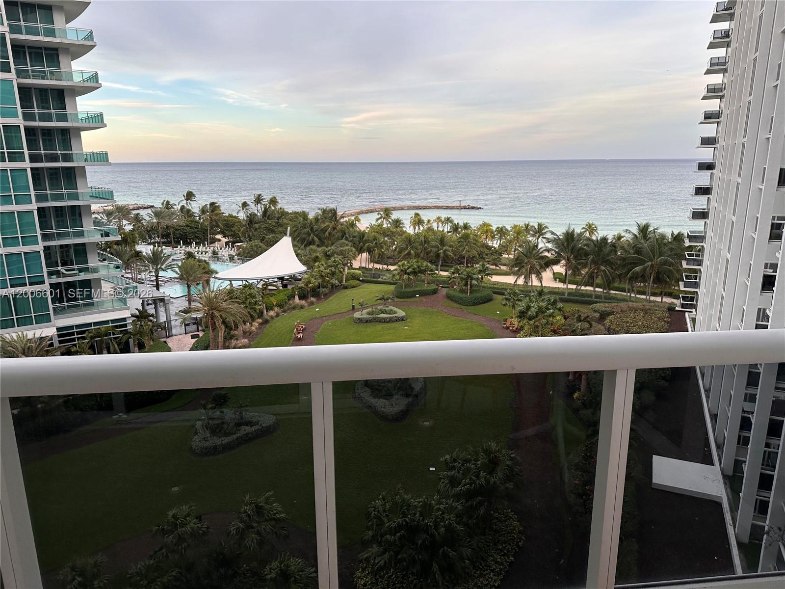 A balcony view overlooks a landscaped courtyard, swimming pool, and the ocean beyond — BAL HARBOUR, FL