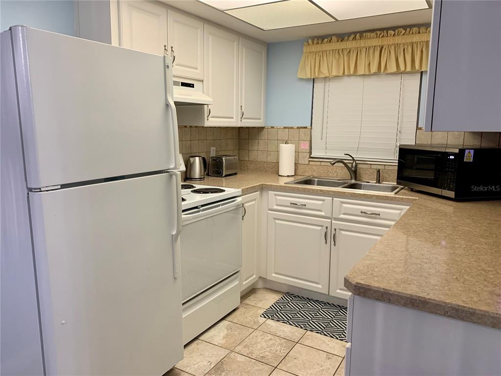 A kitchen features white cabinets, white appliances, a double sink, and tan tiled flooring — 505 66TH AVENUE UNIT 5, ST PETE BEACH, FL