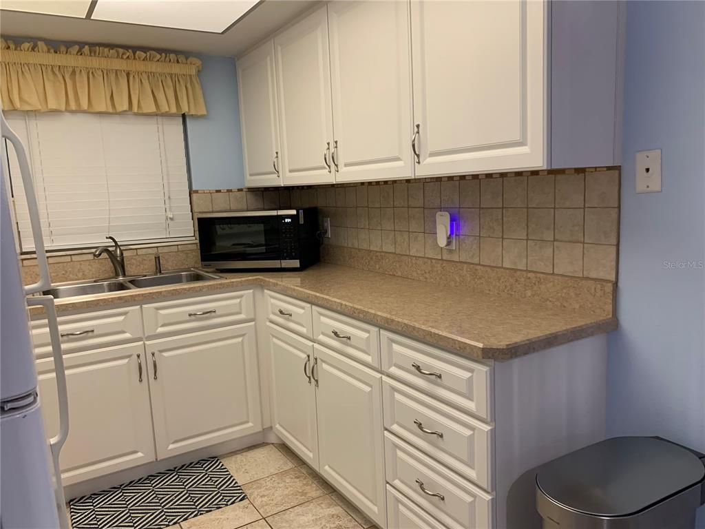 A kitchen features white cabinets, beige countertops, a tiled backsplash, and a stainless steel microwave — 505 66TH AVENUE UNIT 5, ST PETE BEACH, FL