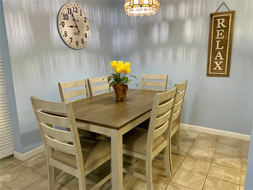 A dining room features a wooden table with six chairs, a wall clock, and a sign — 505 66TH AVENUE UNIT 5, ST PETE BEACH, FL