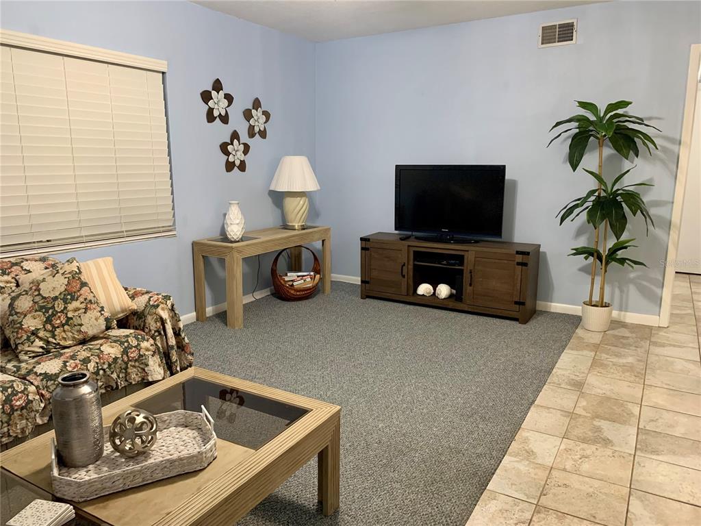 A living room features light blue walls, gray carpeting, a television console, and floral furniture — 505 66TH AVENUE UNIT 5, ST PETE BEACH, FL