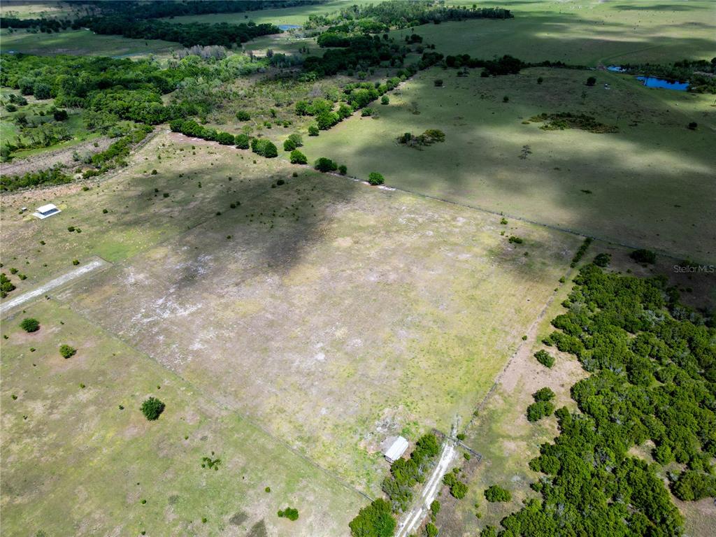 An aerial view shows a large, open grassy field bordered by trees and fencing — 707 CHIHUAHUA ROAD, SEBRING, FL