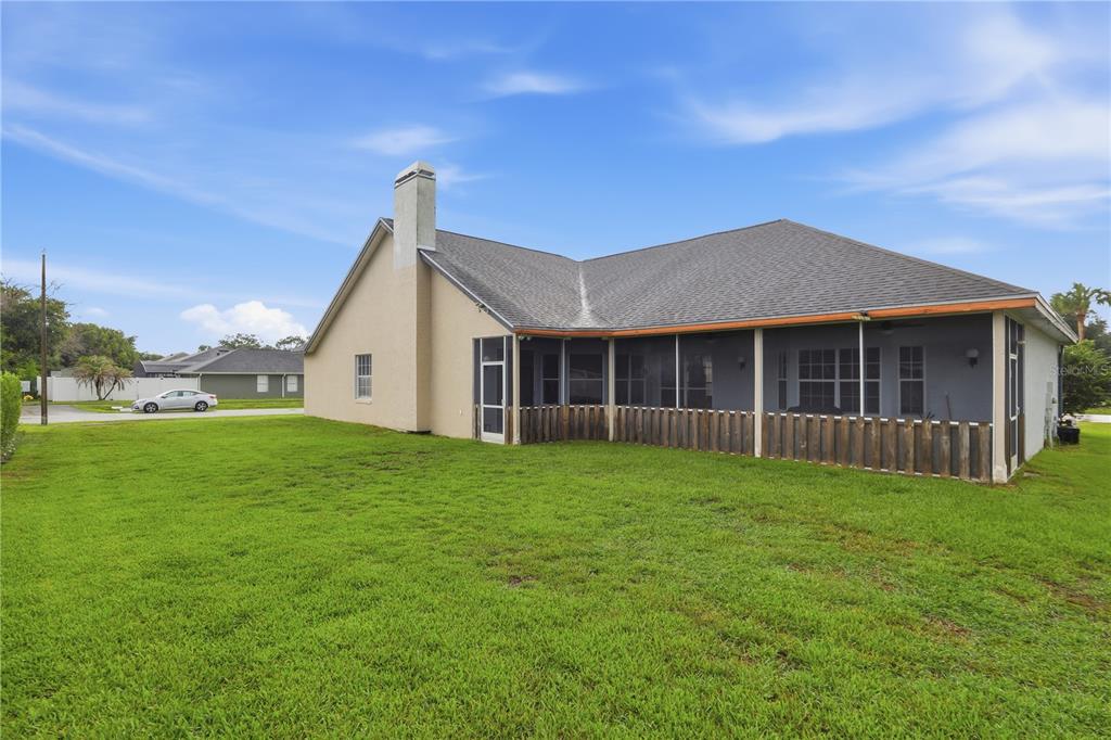 The exterior of a house features a large grassy backyard, a chimney, and a screened-in patio — 20312 MAXIM PKWY, ORLANDO, FL