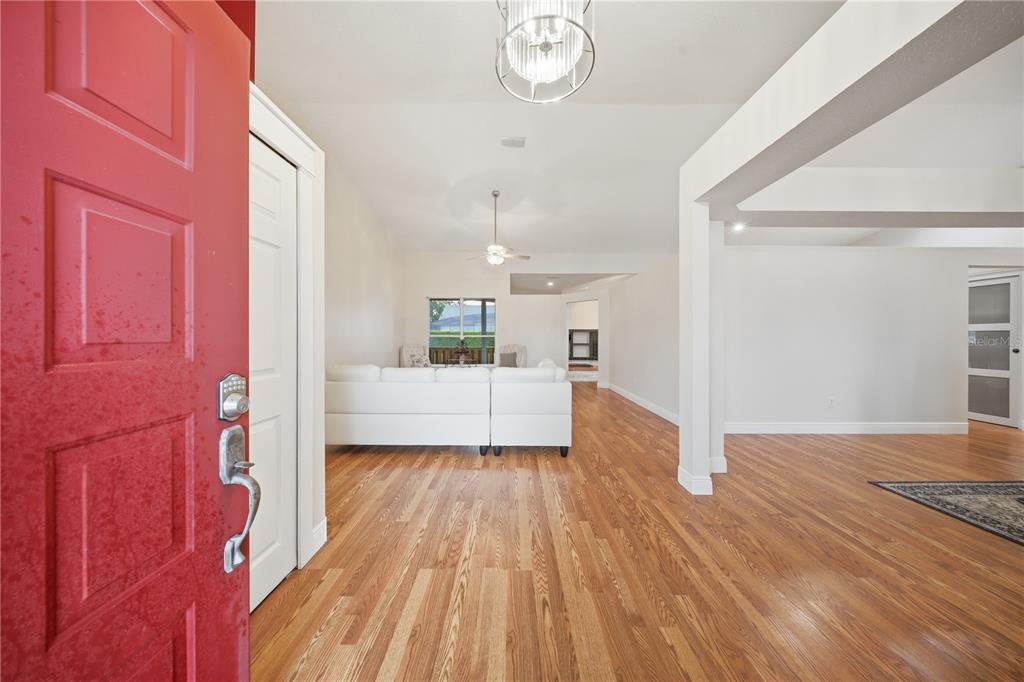 A red front door opens into a living room with hardwood floors and white walls — 20312 MAXIM PKWY, ORLANDO, FL
