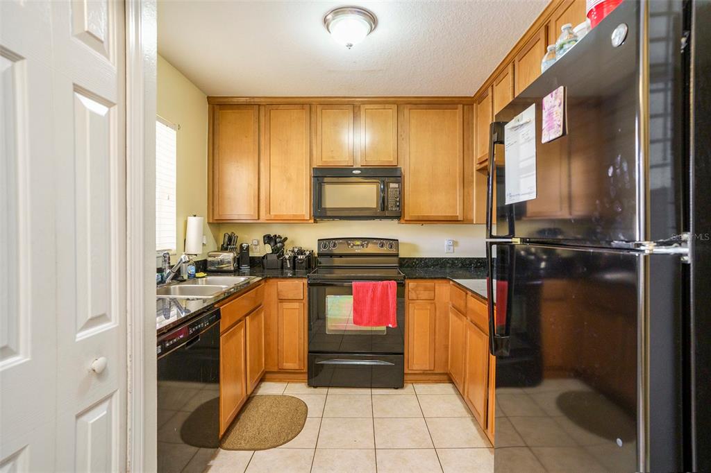 A kitchen features light wood cabinets, black appliances, dark countertops, and light-colored tile flooring — 3869 ISLAND WAY, ST PETERSBURG, FL