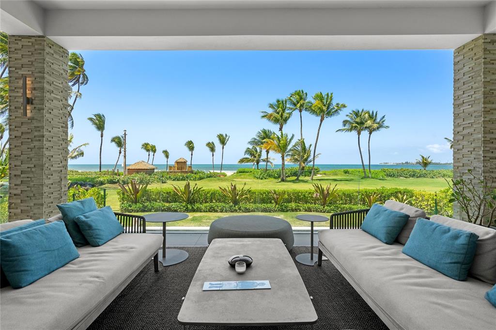 A covered patio features two sofas facing a lawn, palm trees, and the ocean — Bahia Beach Resort OCEAN DRIVE UNIT 3102, RIO GRANDE, PR