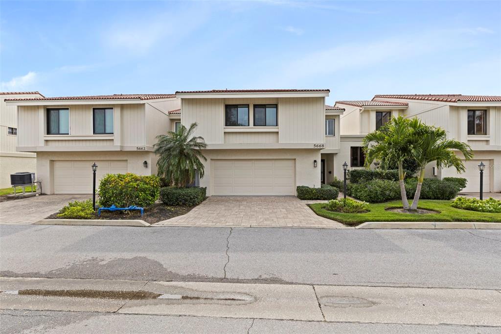 A two-story townhouse exterior features beige vertical siding, a paved driveway, and palm trees — 5668 ESCONDIDA BOULEVARD S, ST PETERSBURG, FL