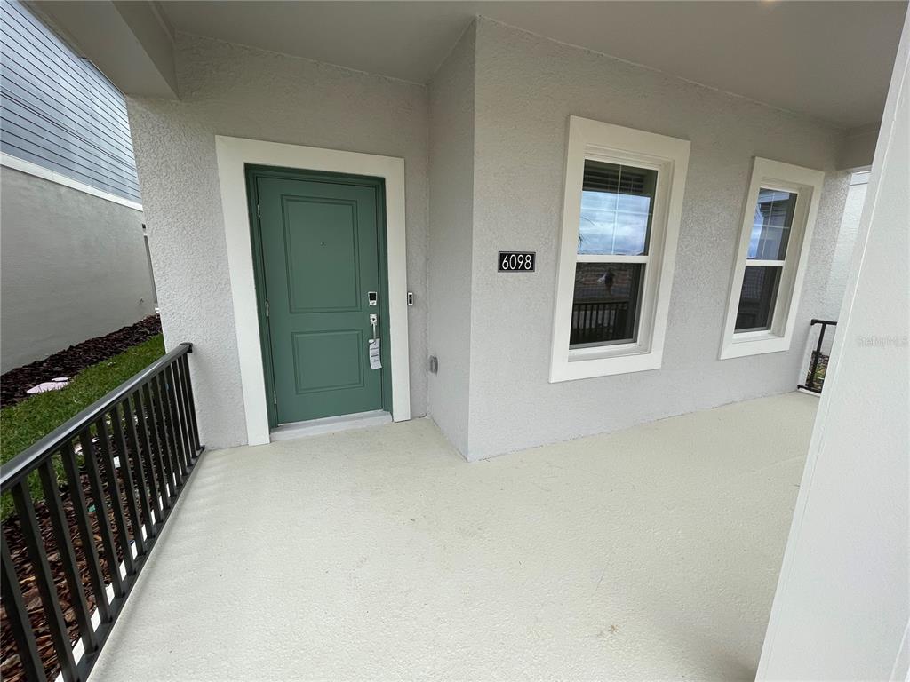A covered porch features a green front door, two windows, and a black metal railing — 6098 BLISSFUL STREET, CLERMONT, FL