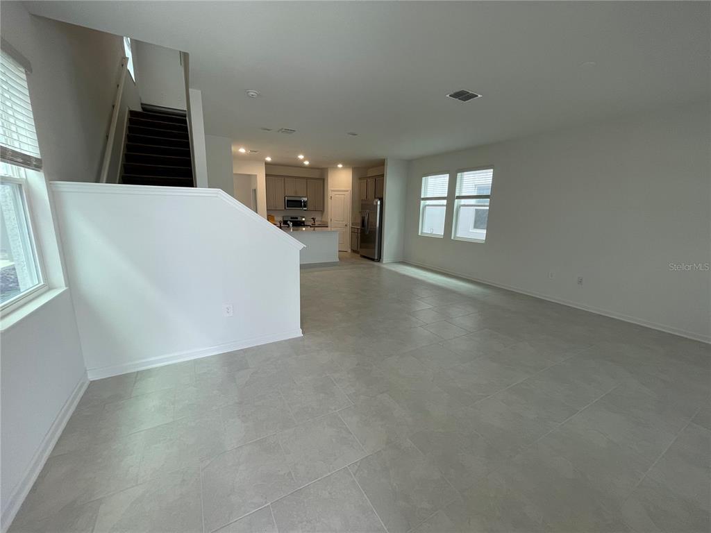 A spacious living area with tile flooring leads to an open kitchen with stainless appliances — 6098 BLISSFUL STREET, CLERMONT, FL