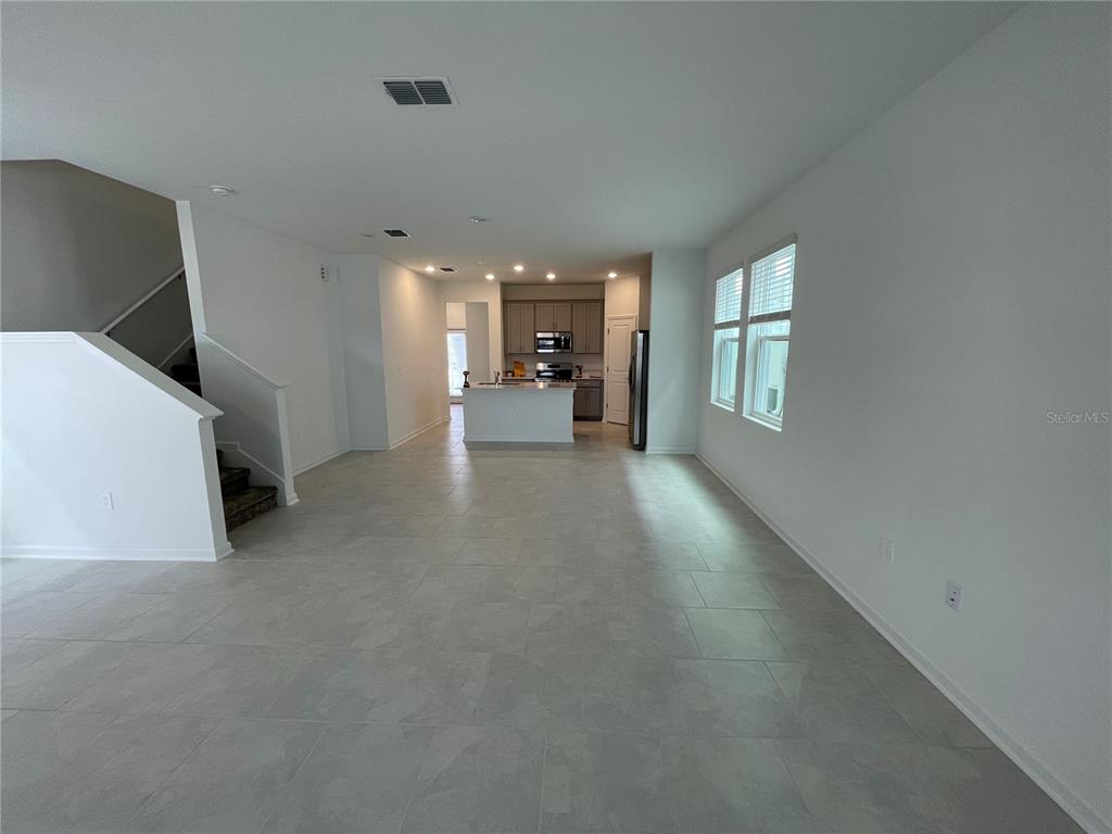 An open-concept living area features light-colored tile flooring, a staircase, and a kitchen island — 6098 BLISSFUL STREET, CLERMONT, FL
