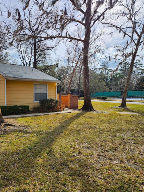A yellow house exterior with a brick wall and a tennis court in the background — 4801 NW 2ND PLACE UNIT K, GAINESVILLE, FL