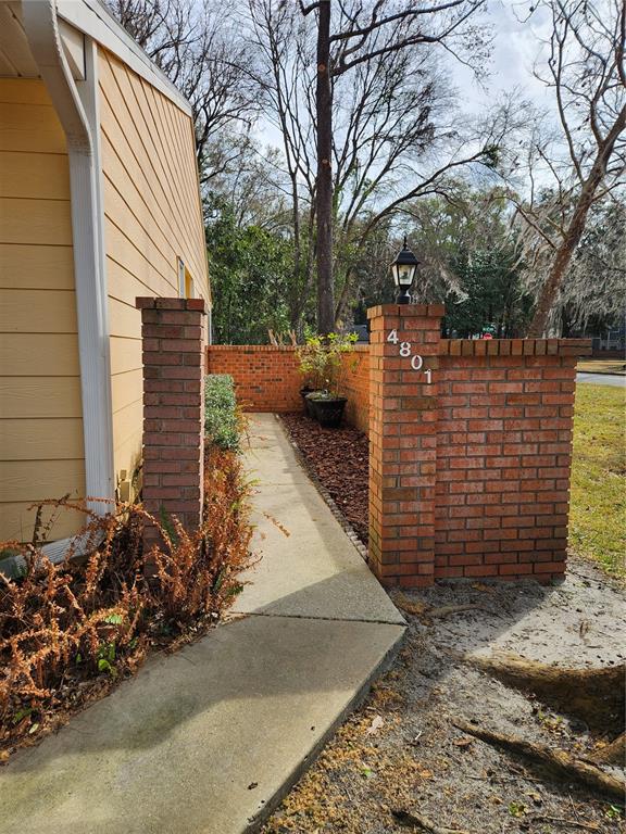 A concrete walkway leads past a brick wall and a yellow-sided house exterior — 4801 NW 2ND PLACE UNIT K, GAINESVILLE, FL