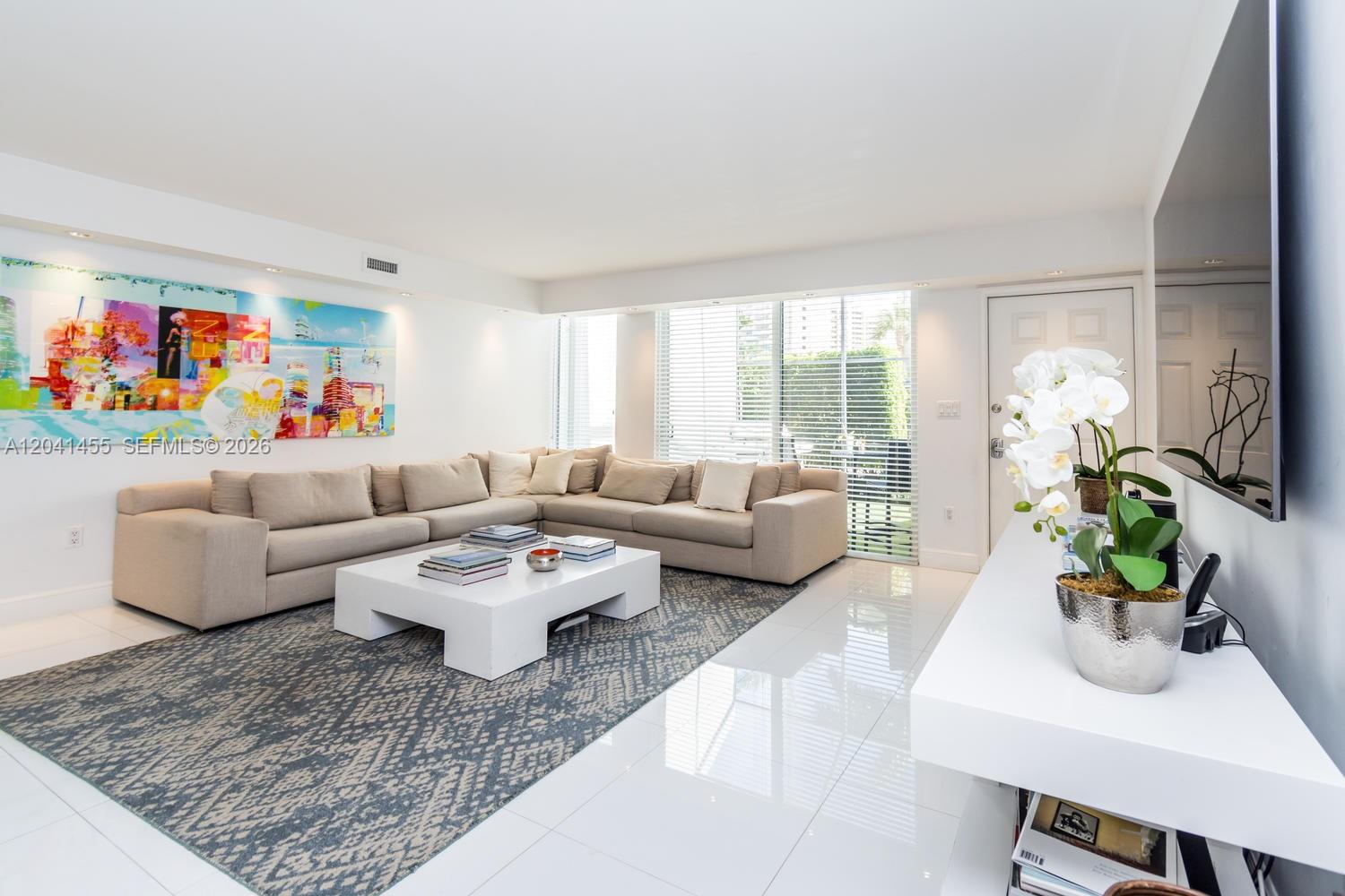 A modern living room features a large sectional sofa, a white coffee table, and colorful wall art — 425 Grapetree Dr # 206, Key Biscayne FL 33149, KEY BISCAYNE, FL