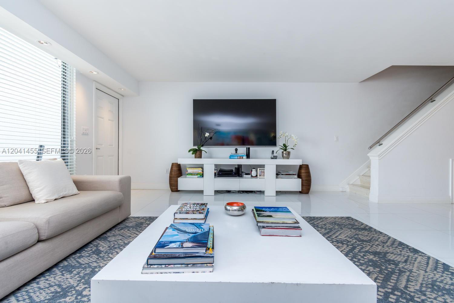 A bright living room features a white media console, a large television, and a coffee table — 425 Grapetree Dr # 206, Key Biscayne FL 33149, KEY BISCAYNE, FL