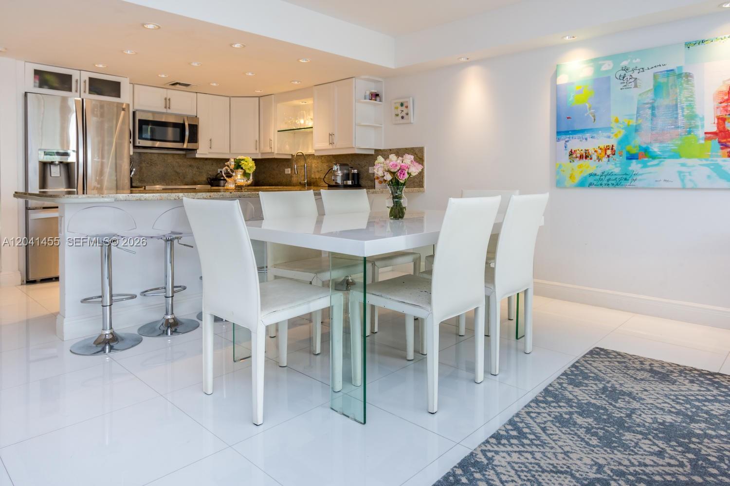 A modern dining area features a white table, white chairs, and an adjacent kitchen — 425 Grapetree Dr # 206, Key Biscayne FL 33149, KEY BISCAYNE, FL