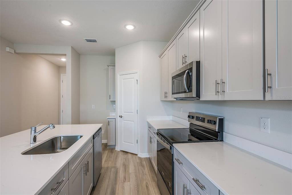 A modern kitchen features light gray cabinets, white countertops, stainless steel appliances, and wood-look flooring — 6140 SW 96TH PLACE, OCALA, FL