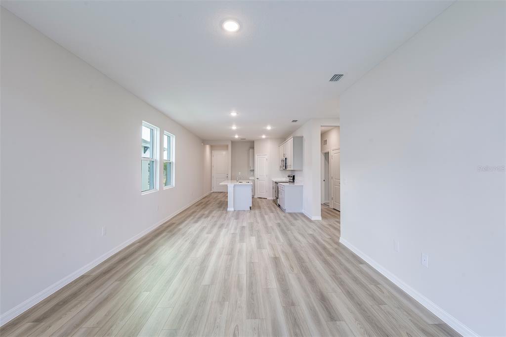An open-concept kitchen and living area features light wood-look flooring and white cabinetry — 6140 SW 96TH PLACE, OCALA, FL