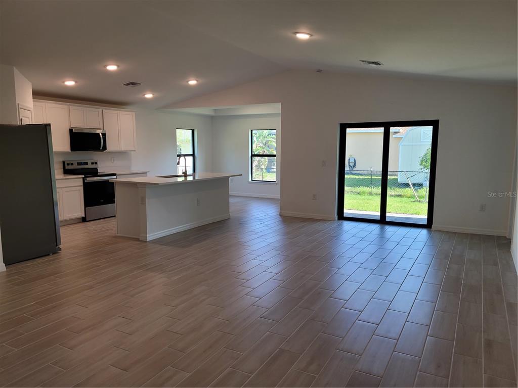 An open-concept kitchen and living area with light wood-look tile flooring and sliding glass doors — 11383 BAGGOT AVENUE, ENGLEWOOD, FL