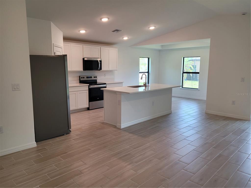 A modern kitchen features white cabinets, stainless steel appliances, a center island, and tile flooring — 11383 BAGGOT AVENUE, ENGLEWOOD, FL