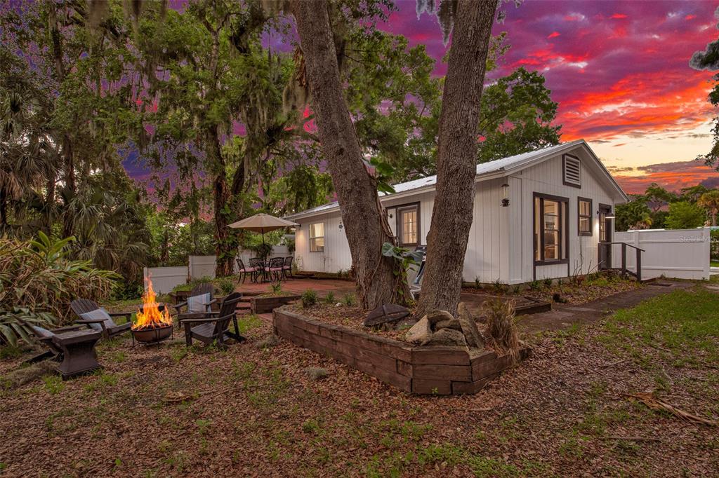 A white house with a fire pit and patio area sits under trees at sunset — 801 CANAL STREET, NEW SMYRNA BEACH, FL