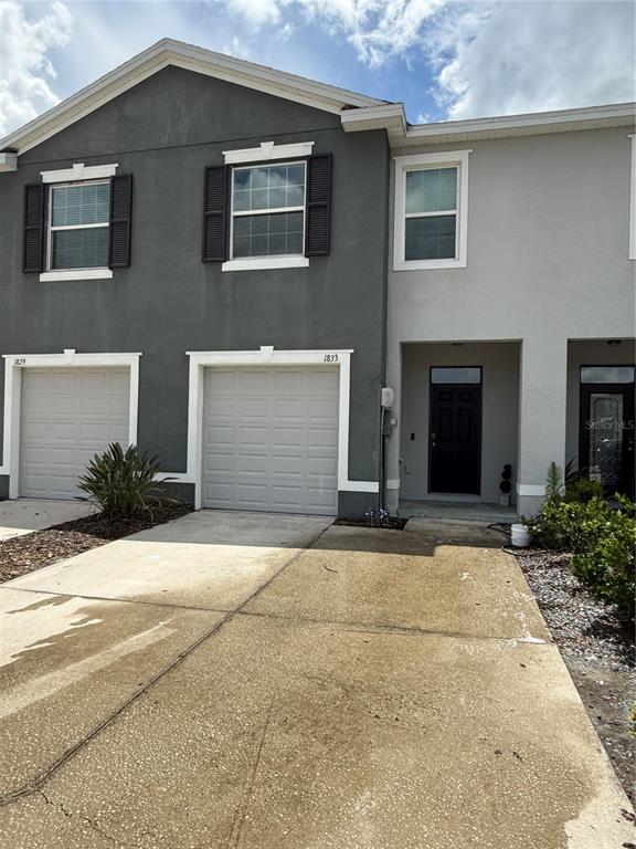 The exterior of a two-story townhouse features a gray facade, two garage doors, and a front entrance — 1833 HOVENWEEP ROAD, WESLEY CHAPEL, FL