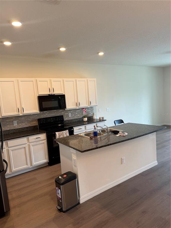 A kitchen features white cabinets, dark countertops, a center island, and a modern light fixture — 1833 HOVENWEEP ROAD, WESLEY CHAPEL, FL