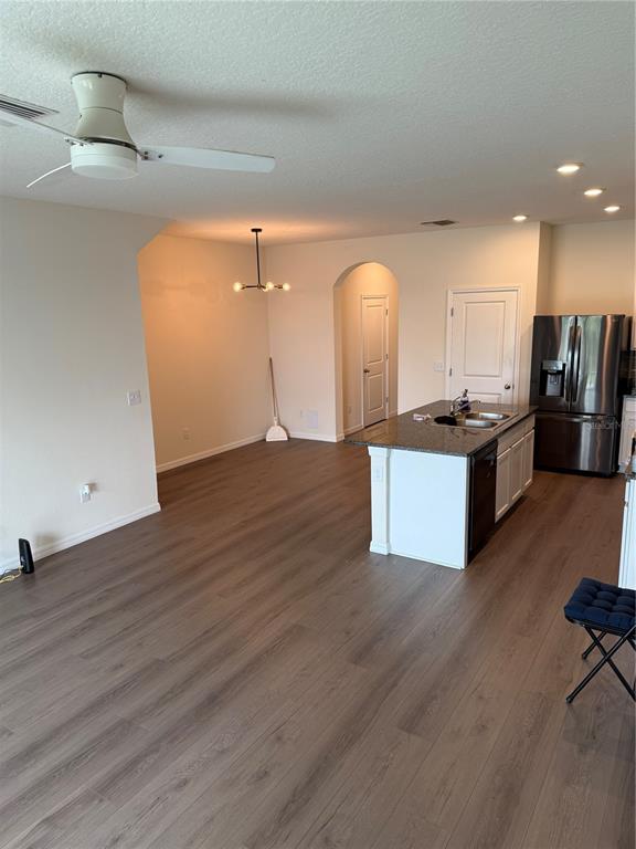 A kitchen with white cabinets, a granite island, and wood-look flooring opens to a living area — 1833 HOVENWEEP ROAD, WESLEY CHAPEL, FL