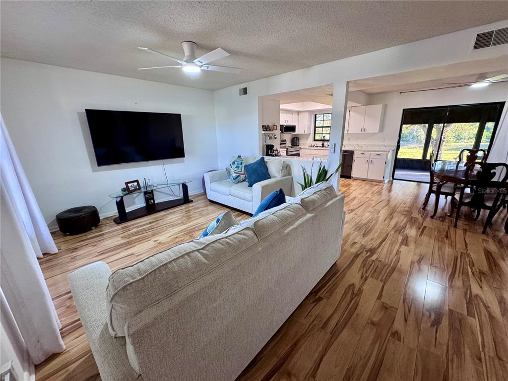 A living room with wood-look flooring, a large television, and an open-concept kitchen — 7186 LEXINGTON CIRCLE, BROOKSVILLE, FL