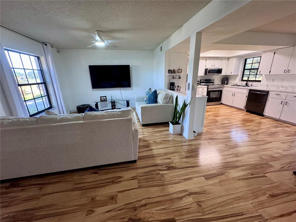 A living room with light-colored sofas and a television opens into a white-cabinet kitchen — 7186 LEXINGTON CIRCLE, BROOKSVILLE, FL