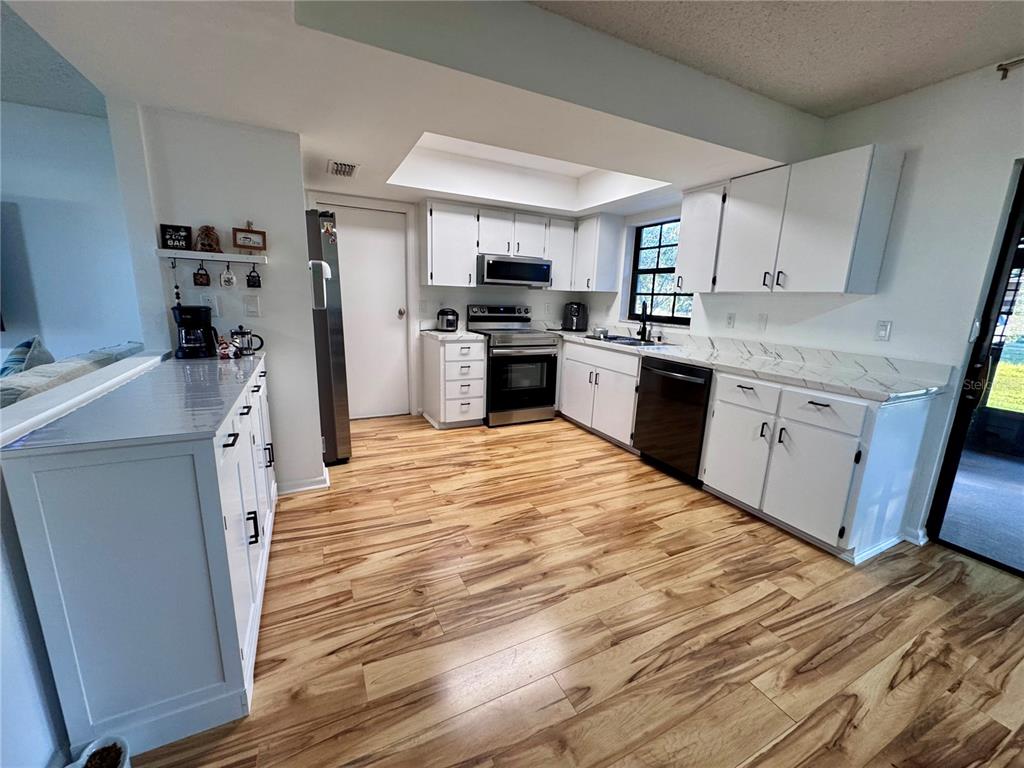 A kitchen features white cabinets, marble-look countertops, stainless steel appliances, and wood-look flooring — 7186 LEXINGTON CIRCLE, BROOKSVILLE, FL