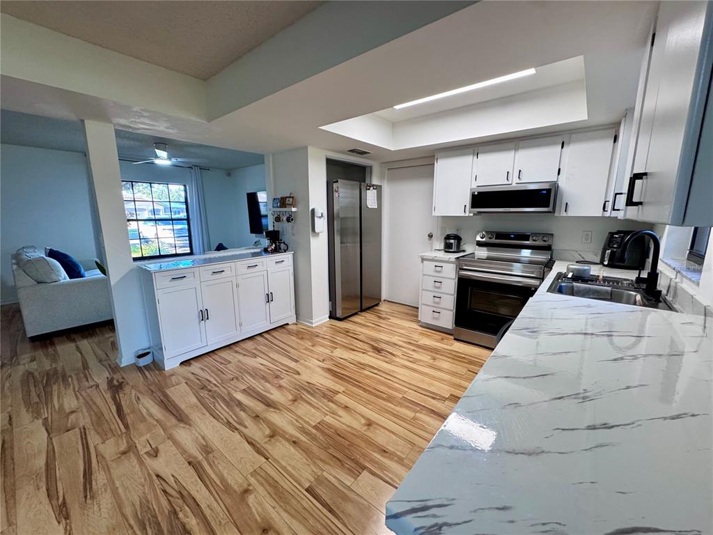 A kitchen with white cabinets, marble-patterned countertops, and wood-look flooring opens to a living area — 7186 LEXINGTON CIRCLE, BROOKSVILLE, FL