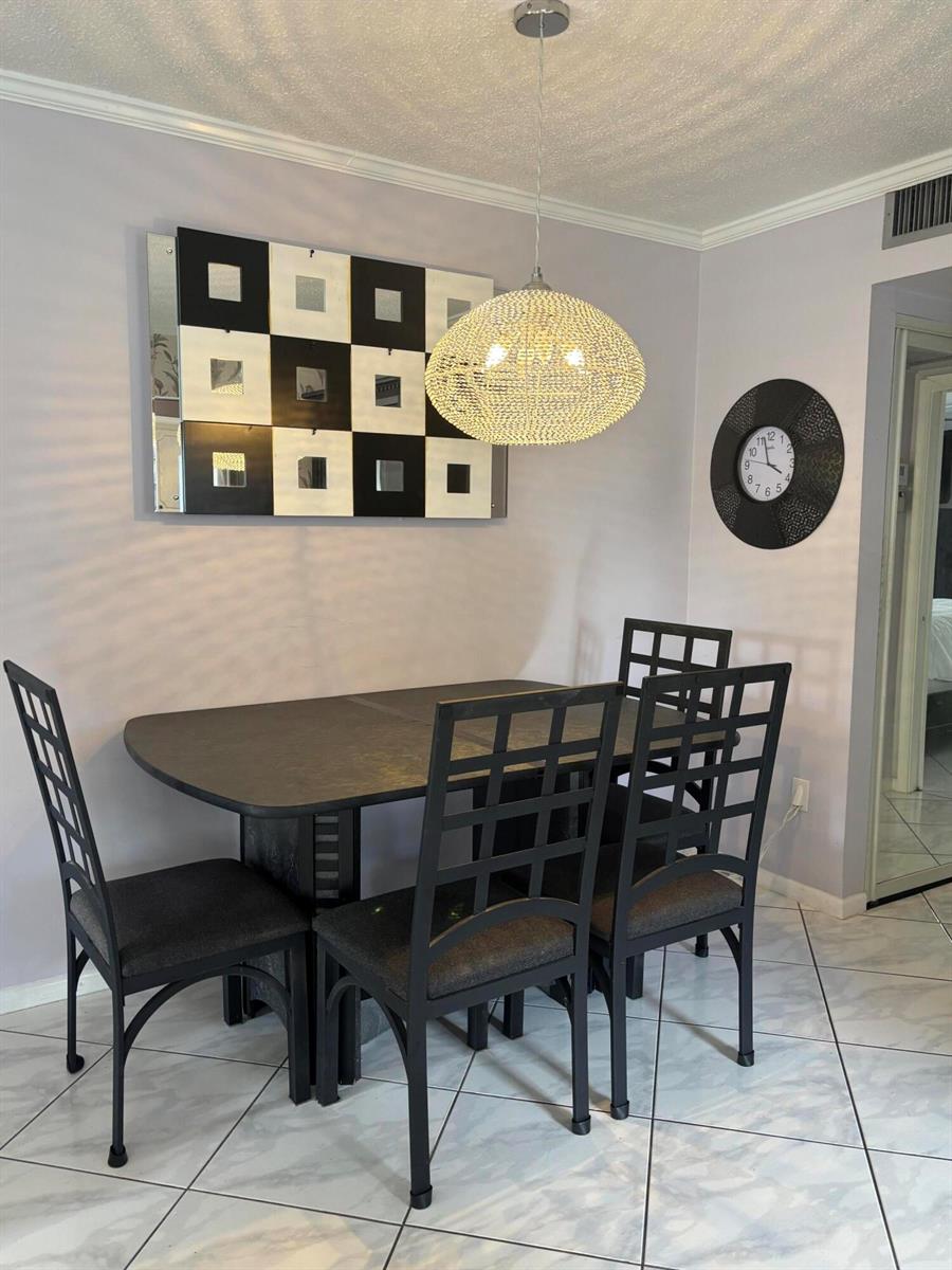A dining room features a dark table, four grid-back chairs, a crystal pendant light, and wall art — 81 Windsor D, West Palm Beach FL 33417, WEST PALM BEACH, FL
