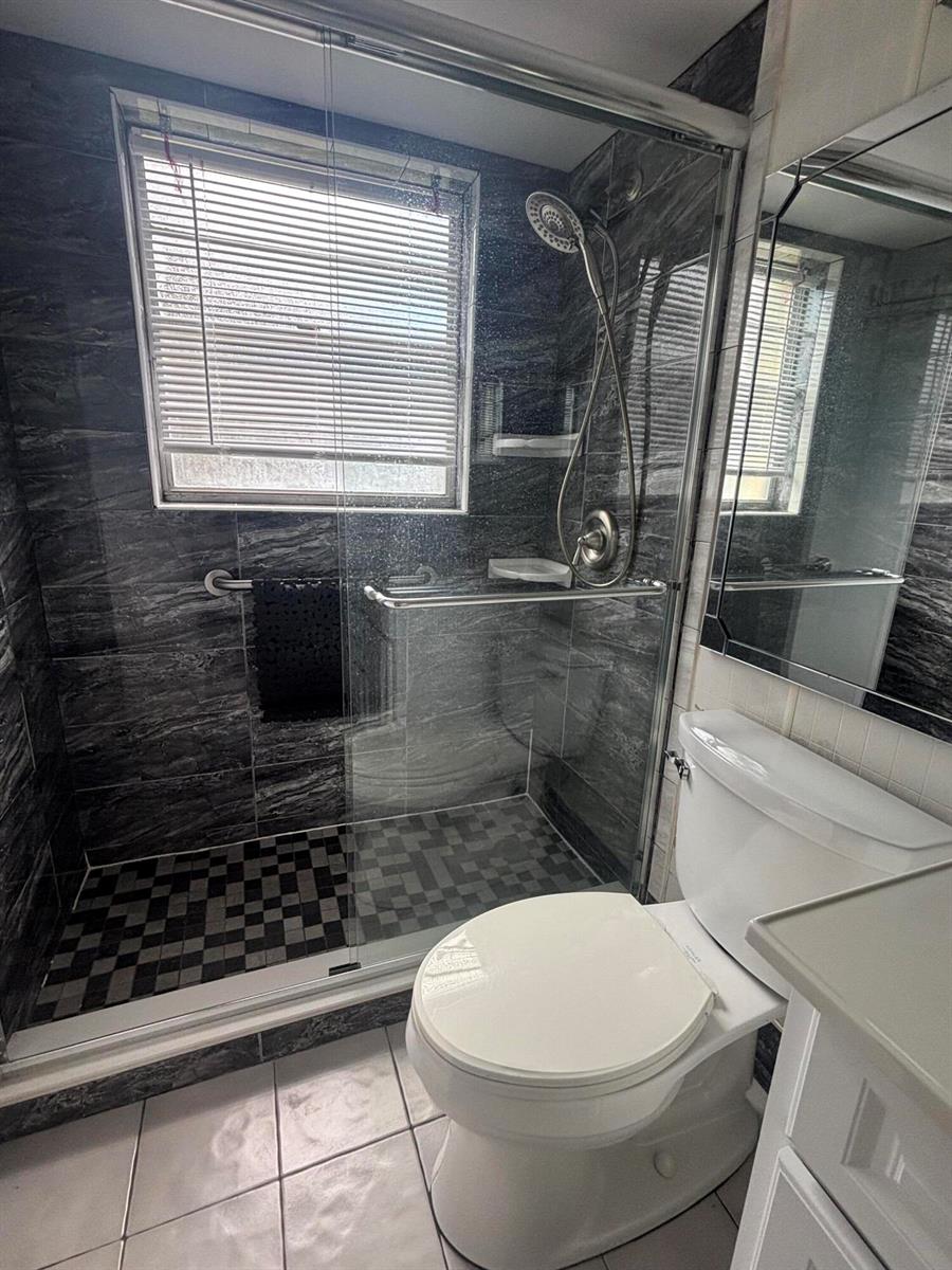 A bathroom features a glass-enclosed shower with dark marble-patterned tile and a white toilet — 81 Windsor D, West Palm Beach FL 33417, WEST PALM BEACH, FL