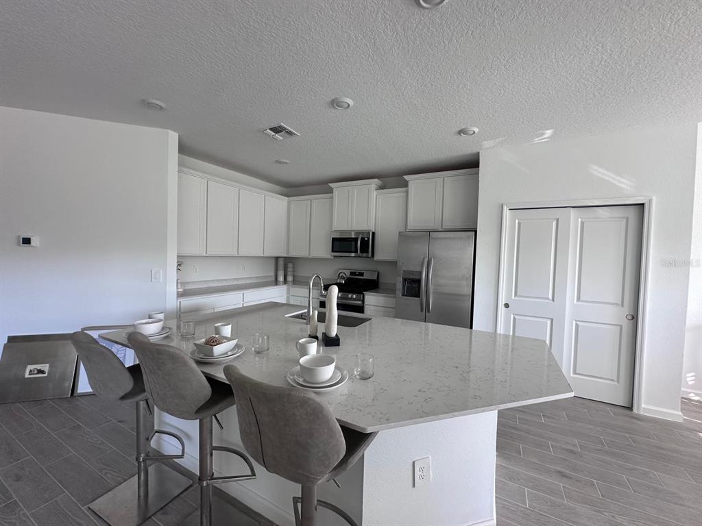 A modern kitchen features white cabinets, stainless steel appliances, and a large quartz-topped island — 12345 NW 137 WAY, ALACHUA, FL