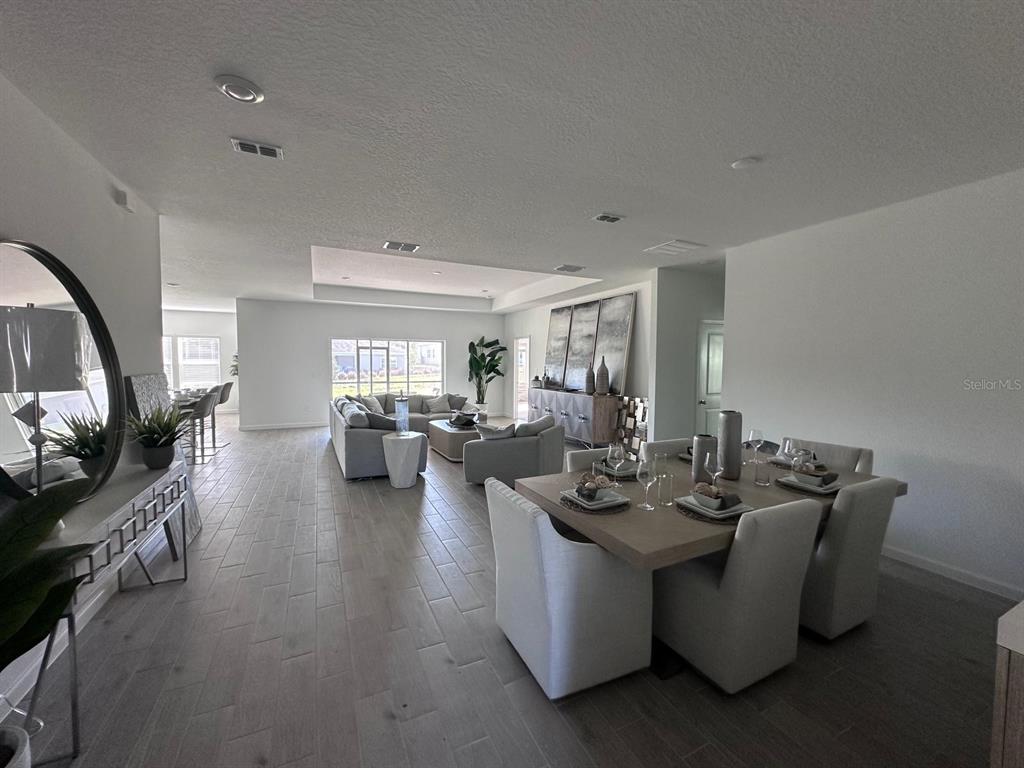 An open-concept living and dining area features light wood-look tile flooring and neutral furniture — 12345 NW 137 WAY, ALACHUA, FL